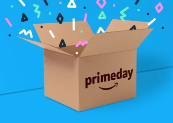 A brown box with "primeday" and the Amazon logo on it is open against a bright blue background. Colorful geometric shapes are floating around, giving a festive feel, emphasizing the excitement of shopping on Amazon. | FintechZoom
