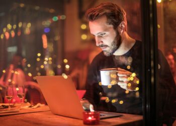 Man Holding Mug in Front of Laptop | FintechZoom