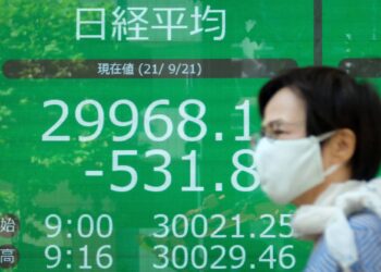 A pedestrian walks past an electronic quotation board displaying share prices of the Tokyo Stock Exchange in Tokyo