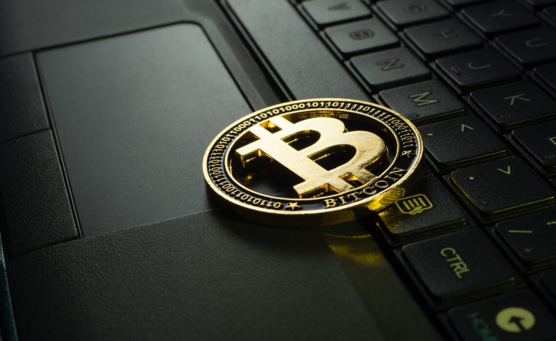 Golden Bitcoin over black laptop | FintechZoom
