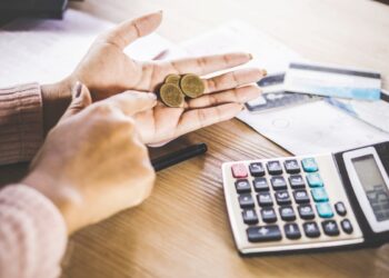 Person using a calculator and coins in hand | FintechZoom
