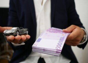Man in money and car toy in hands | FintechZoom