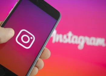 Person with Instagram app open in mobile with a pink background with White Instagram Logo | FintechZoom