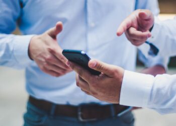 Man showing his mobile to another man | FintechZoom