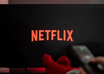 netflix logo on a smart tv and a person holding a remote | FintechZoom
