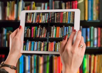 Person taking picture of books in library using a white tablet | FintechZoom
