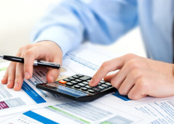 Man filling papers and using a calculator | FintechZoom