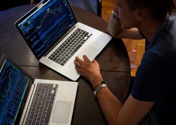 Man trading on 2 laptop - FintechZoom