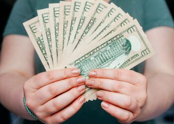 Person holding 10 dollar bills american currency | FintechZoom