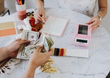 Persons counting money on white table | FintechZoom