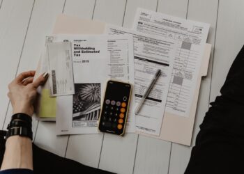 Person holding Tax Papers and pen near calculate | FintechZoom