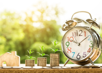 On Table: clock, a little wood house and coins with seeds | FintechZoom