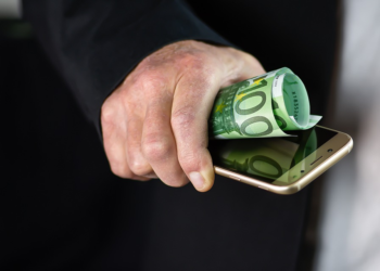 Man holding mobile and money on his hand | FintechZoom