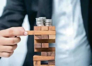 Man playing with tower wood elements with coins at top | FintechZoom