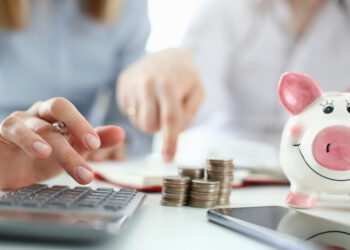 Man and woman hand consider on calculator expenses of family budget with Pig Money on table| FintechZoom
