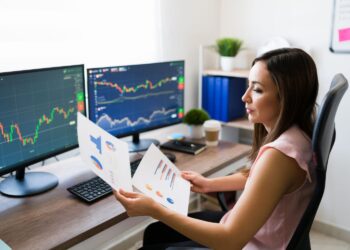 Woman looking for investment charts in paper and on screen | FintechZoom