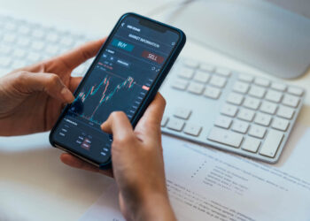 Person holding in hands mobile phone wit stock market app | FintechZoom