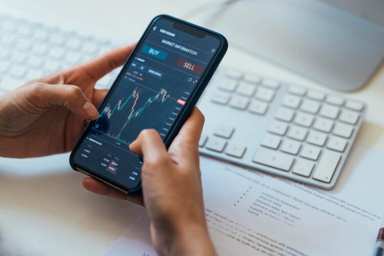 Person holding in hands mobile phone wit stock market app | FintechZoom