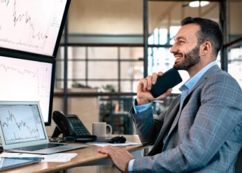 Man looking to computer and holding a phone | FintechZoom