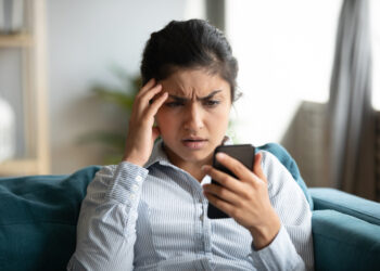 Confused millennial Indian girl sit at home look at cellphone having operational problems | FintechZoom