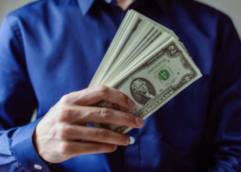 Man with blue shirt holding dollar notes | FintechZoom