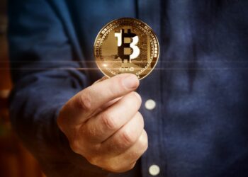 Man holding a golden bitcoin | FintechZoom