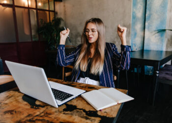laughing woman in sunglasses working with computer | FintechZoom