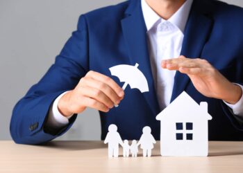 Man Protecting with his hands a house and a family toy | FintechZoom