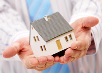 Man holding in his hands a tiny white house | FintechZoom