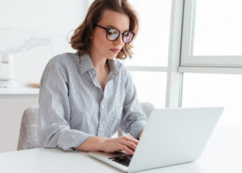 Young woman texting email on laptop while sitting at table in light room | FintechZoom