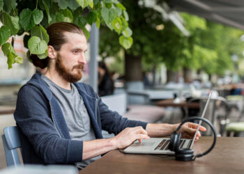 photo side view of man with laptop and headphones at city terrace | FintechZoom