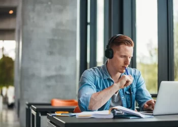Student-at-library-looking-at-laptop-and-thinking | FintechZoom