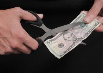 Person with scissors hand cutting money in a black background | FintechZoom