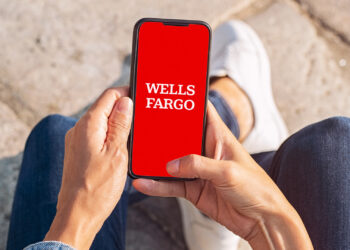 Closeup of young woman hand holding mobile phone with Wells Fargo APP | FintechZoom