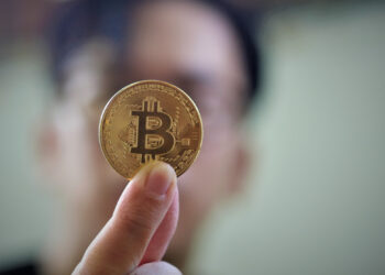 Man holding one bitcoin | FintechZoom