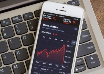 Smartphone with red Dow Jones Chart over Laptop keyboard | FintechZoom