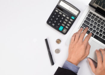 Businessman sitting with open laptop and calculator | FintechZoom