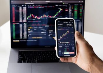 Person Trading in Stock Market using Laptop and Smartphone | FintechZoom