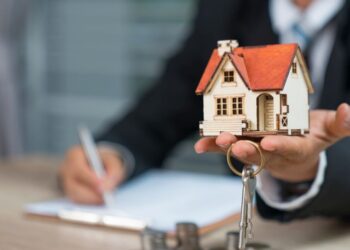 Man sign a document and in other hand holding a little house | FintechZoom