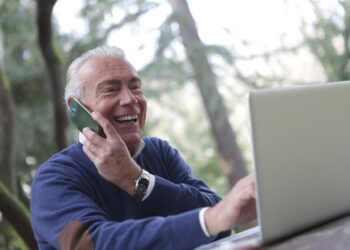 Elderly Man in Blue Long Sleeve Sweater Using Cellphone | FintechZoom