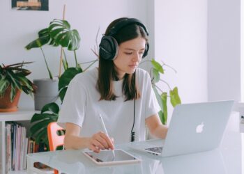 Woman In White Shirt Using Silver Macbook and headphones | FintechZoom