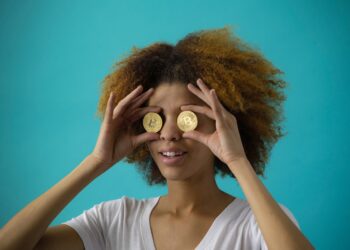 Woman Holding Two Bitcoins near her eys like glasses | FintechZoom