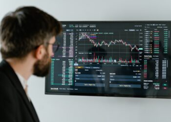 Man in Black Suit Standing in Front of Black Monitor wit Trading Charts | FintechZoom