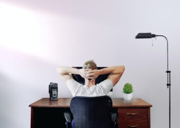 Man holding his head while sitting on chair near computer desk | FintechZoom
