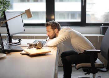 Man in White Shirt Sitting on Chair and tired in front of his computer | FintechZoom