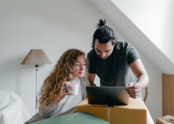 Focused couple browsing laptop on cardboard box | FintechZoom