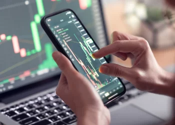Man trading on mobile and laptop | FintechZoom