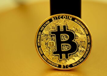 A golden black bitcoin coin stand in front of the pole | FintechZoom