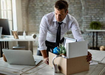 Sad entrepreneur packing his belongings in cardboard box while leaving the office | FintechZoom