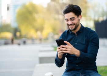 Young man using a mobile phone while standing outdoors | FintechZoom